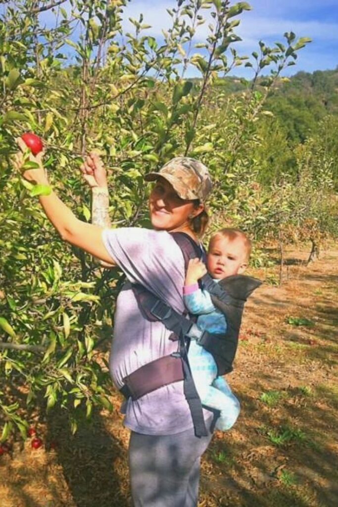 Woman carrying a baby on her back picks an apple